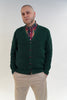 Man wearing a green cardigan over a plaid shirt with beige pants on a white background
