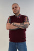 Man wearing a maroon sweater with plaid sleeves and blue jeans against a plain background