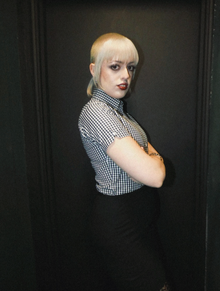 Person with a shaved head wearing a checkered shirt against a dark background