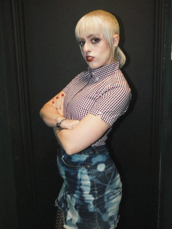 Person wearing a checkered shirt and denim overalls against a black background